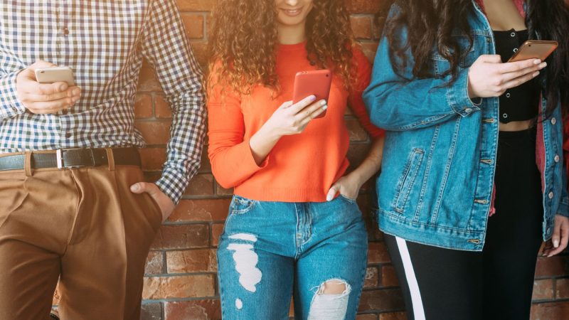 Millennials communication problem. Young people standing in row, chatting in social networks online, ignoring each other.